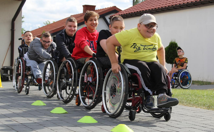 Sześcioro chłopców na wózkach inwalidzkich stworzyło pociąg - jadą jeden za drugim. Uśmiechnięci, widać, że dobrze się bawią!